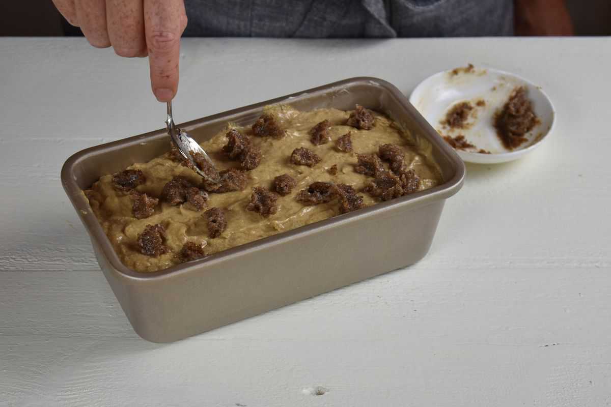 butter and sugar mixture being dropped onto the top of the batter in a loaf pan