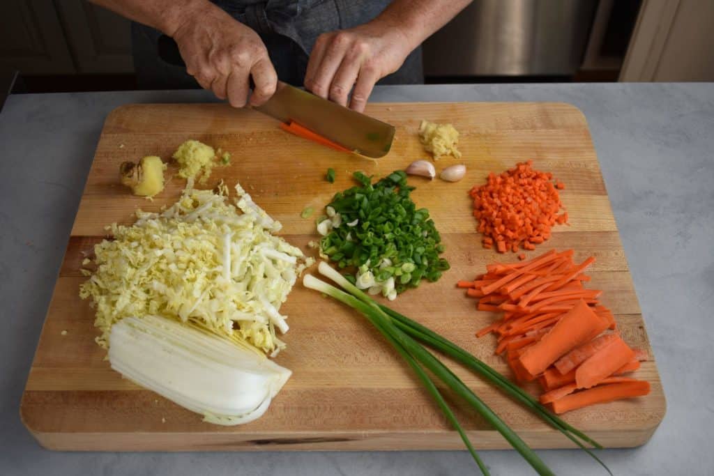 napa cabbage, carrots, scallions and ginger chopped on a wooden chopping board.