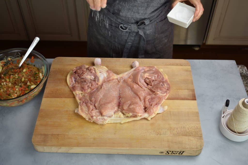 the deboned chicken being seasoned with salt.