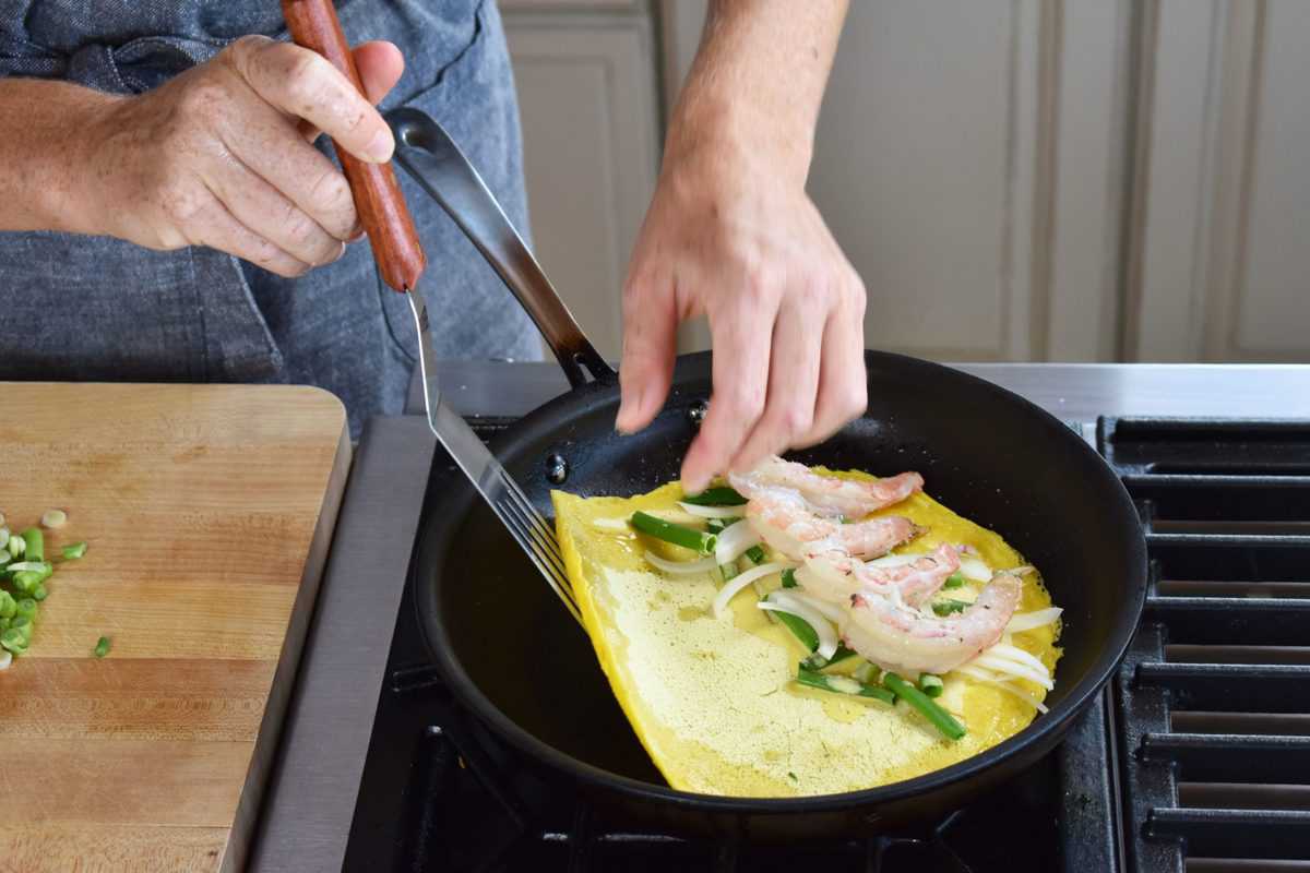 shrimp and scallions added to the crepe and being folded in a skillet.