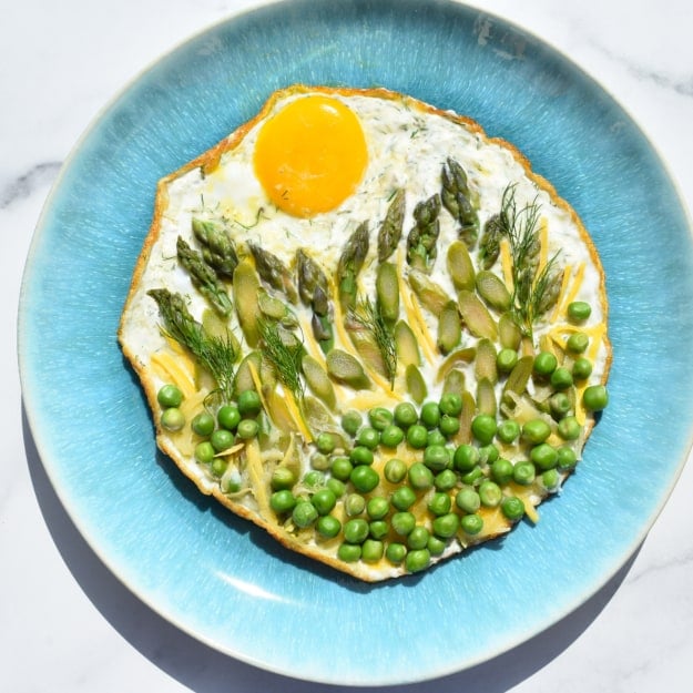 overhead shot of a fried egg, peas, asparagus arranged to look like a sunrise