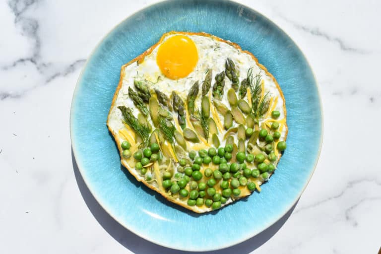 overhead shot of a fried egg, peas, asparagus arranged to look like a sunrise