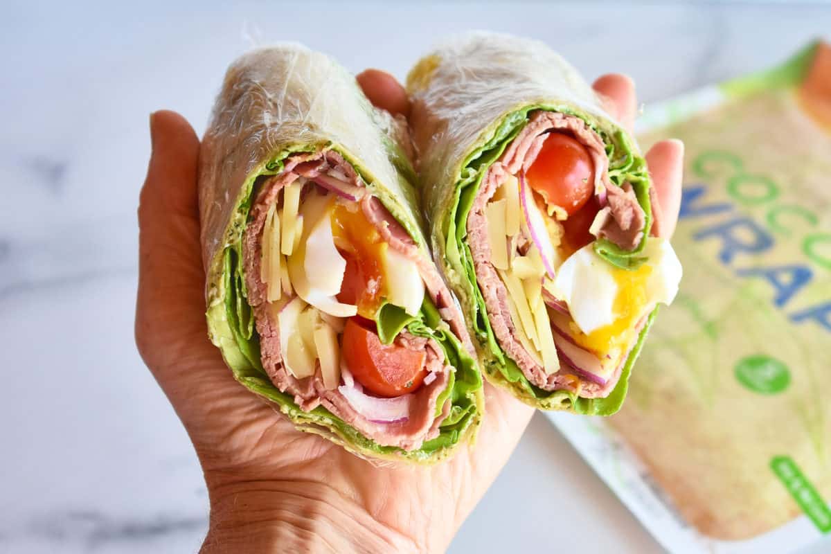 a hand holding two pieces of a roast beef wrap showing the filling