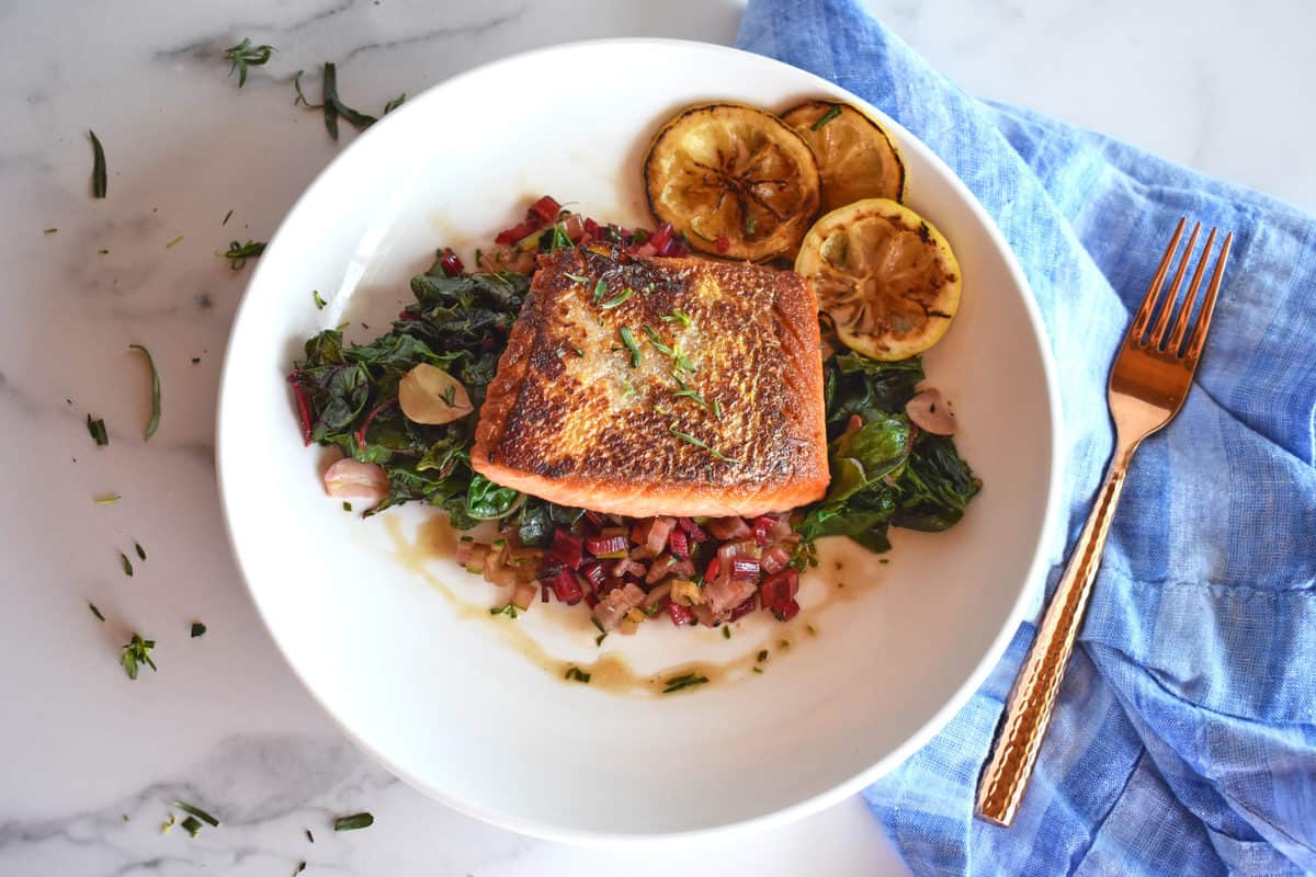 seared salmon on a plate on a bed of chard with lemon slices