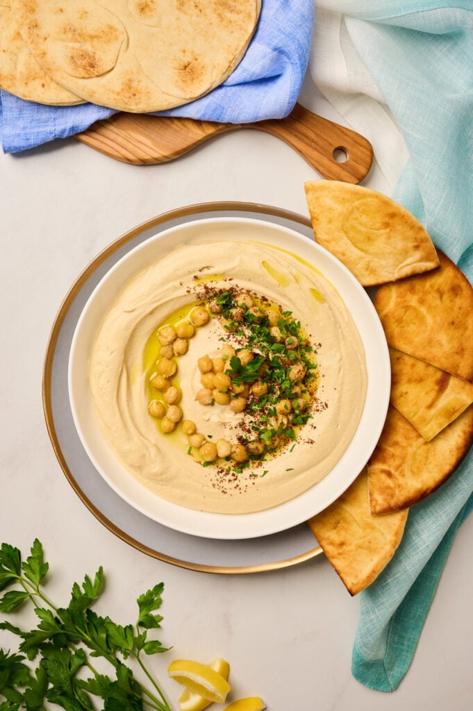 Finished bowl of hummus topped with chickpeas, sumac, olive oil, and parsley served with pita