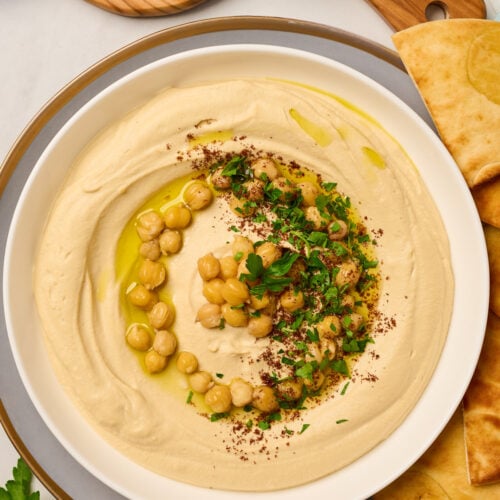 Close-up of creamy hummus garnished with chickpeas, sumac, olive oil, and parsley