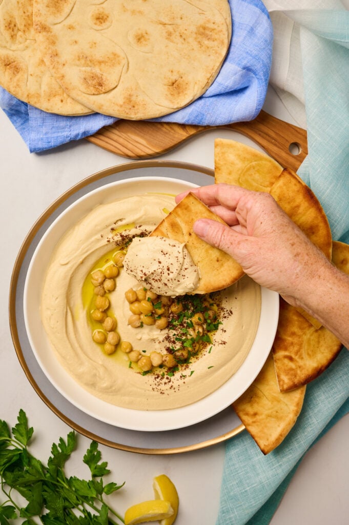 Hand dipping toasted pita into creamy hummus topped with olive oil and spices