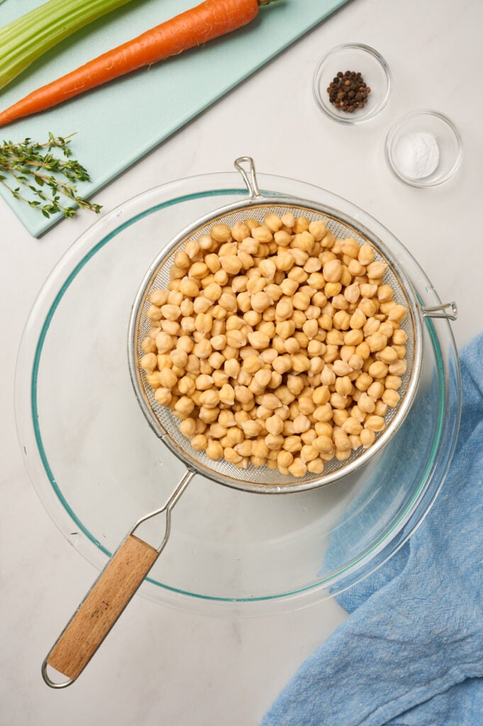 Strained cooked chickpeas in a fine mesh sieve over a glass bowl