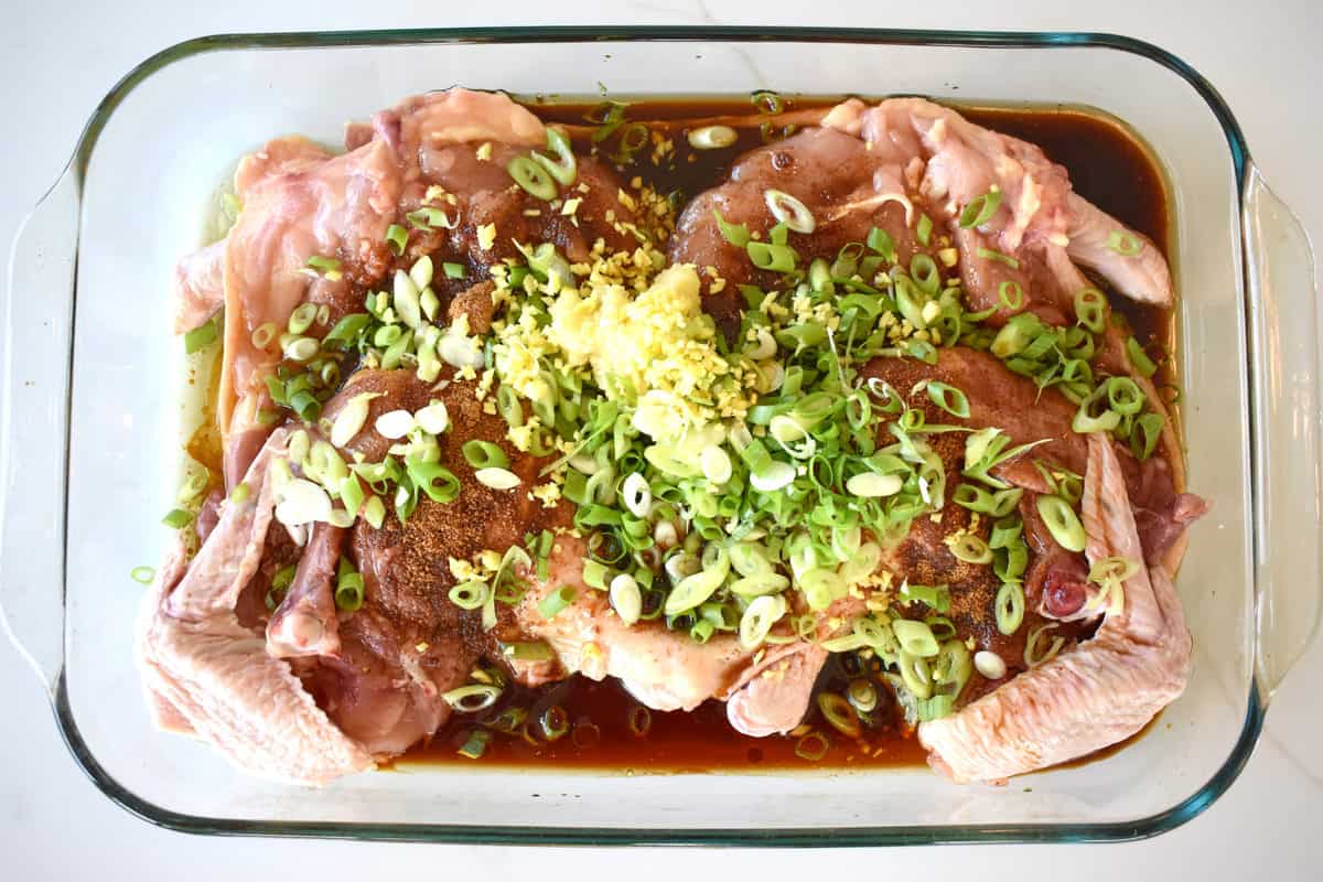 raw chicken, soy sauce, green onions and ginger in a glass roasting tray