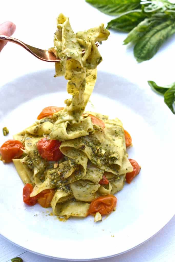 Homemade Pappardelle Pasta with tomatoes and pesto on a plate with a fork of pasta