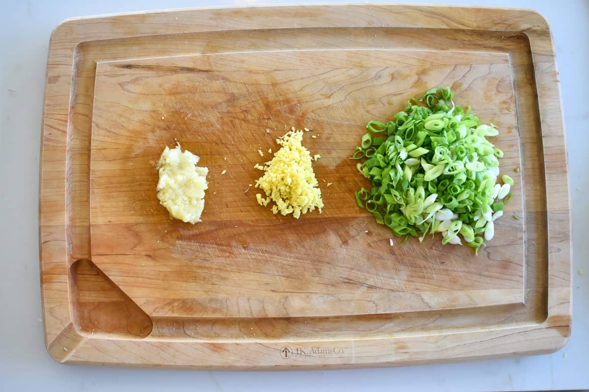 garlic, ginger and sliced green onions on a wooden chopping board