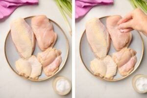 Hand seasoning chicken breasts and thighs with salt, arranged on a blue plate, styled with green onions and pink linen in the background.