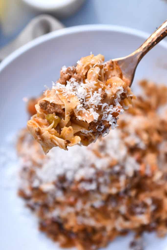 close up shot of a fork with pasta bolognese covered in shredded parmesan cheese