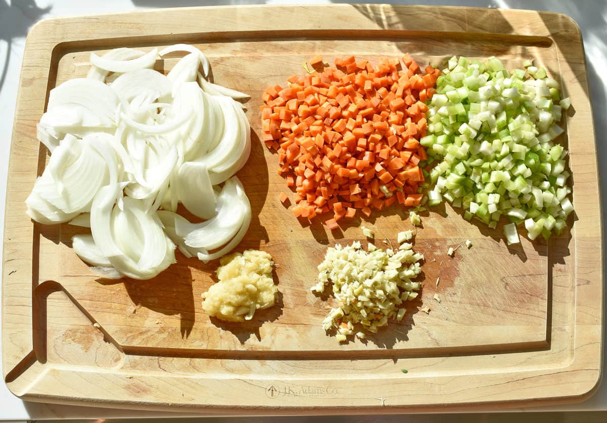 a chopping board with sliced onion, garlic, ginger, green onions and carrot