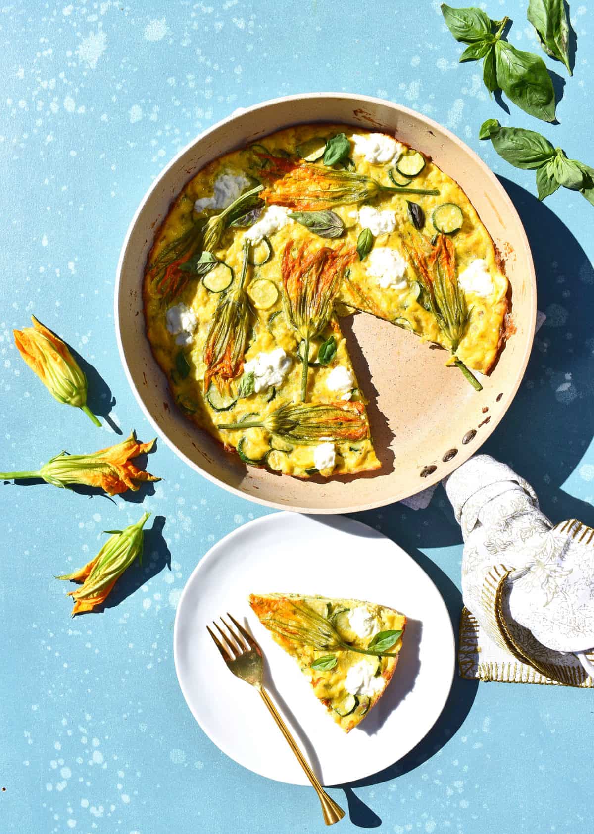 overhead shot of squash blossom and goat cheese frittata with a slice taken out, a plate with a slice of frittata and squash blossoms