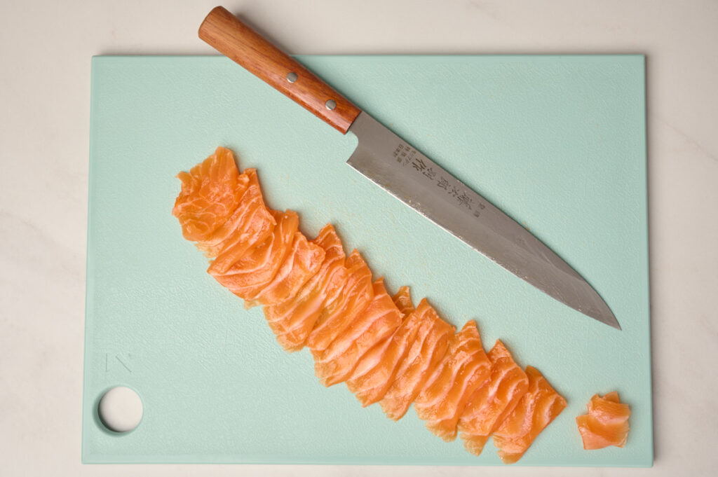 All pieces of salmon sashimi cut using the Sogigiri method lined up with the Yanagiba knife on a blue cutting board.