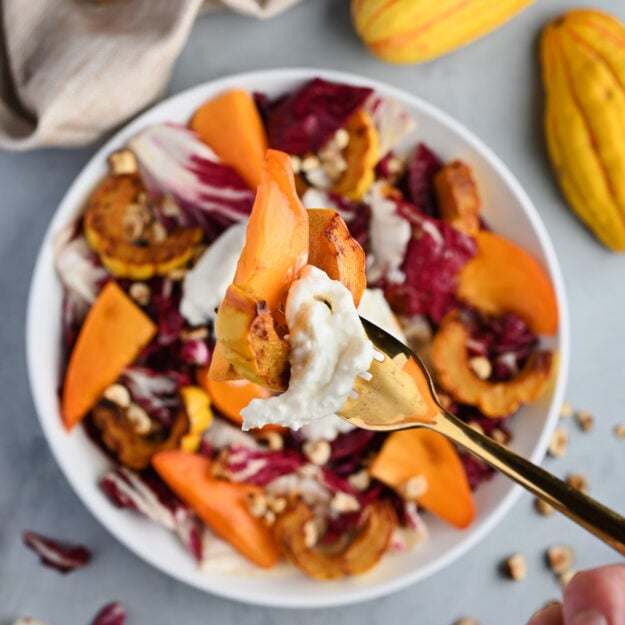 Hand holding a fork with a bite of persimmon salad over the plated dish.
