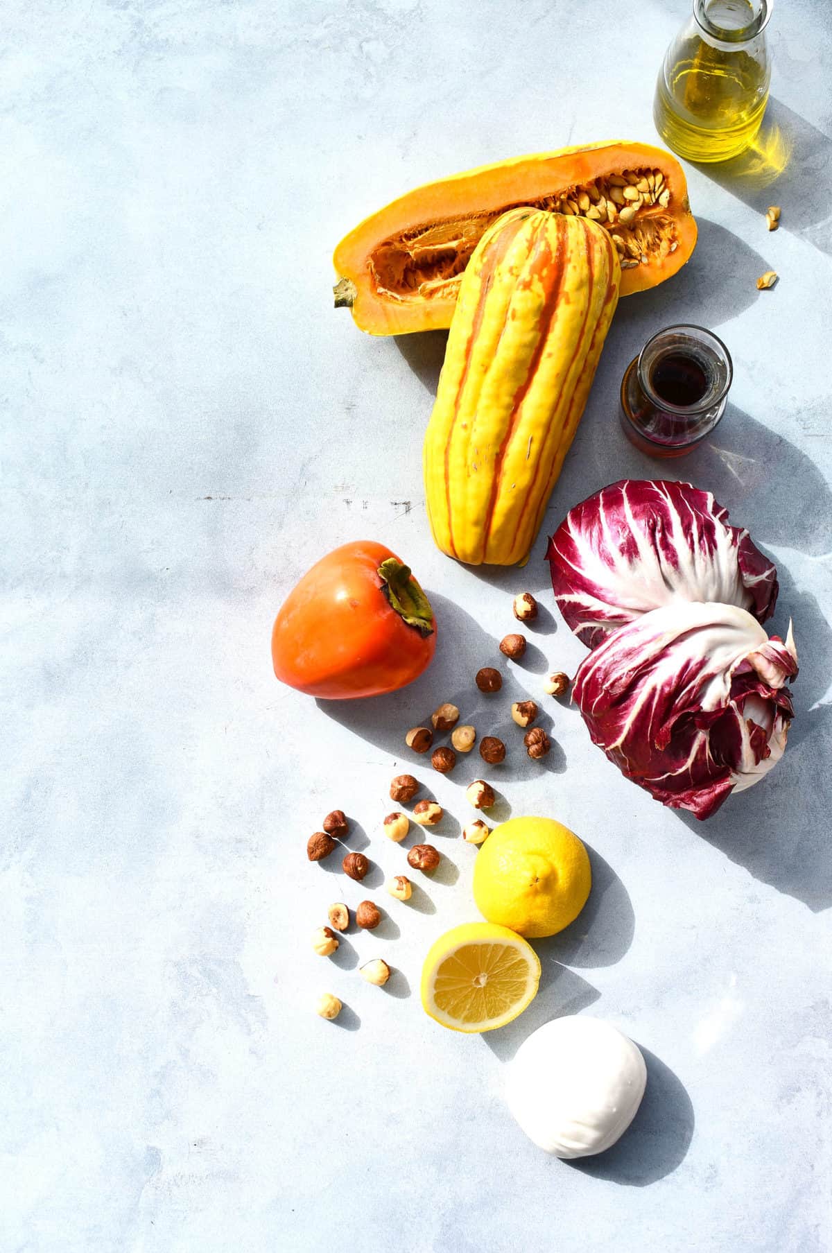 overhead shot of ingredients for salad: squash, persimmon, lemon, burrata and olive oil