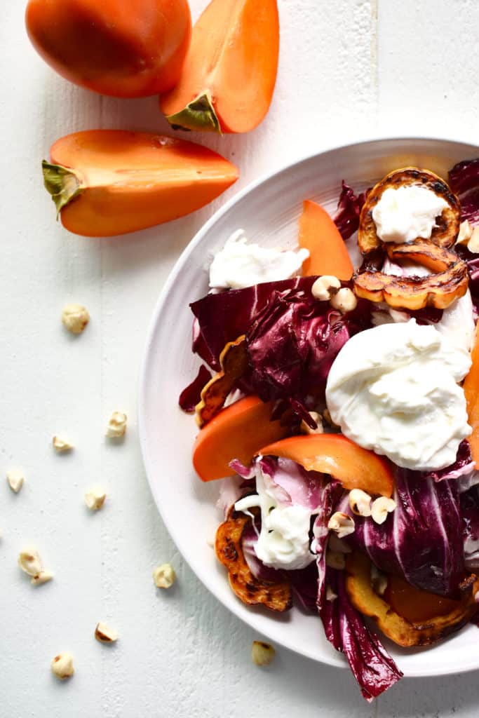 overhead shot of salad with burrata cheese and sliced persimmon.