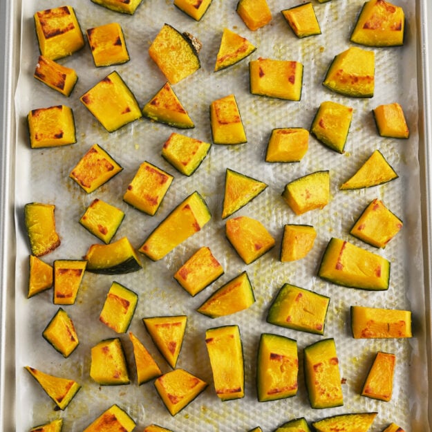 Roasted kabocha squash on a parchment-lined sheet tray.