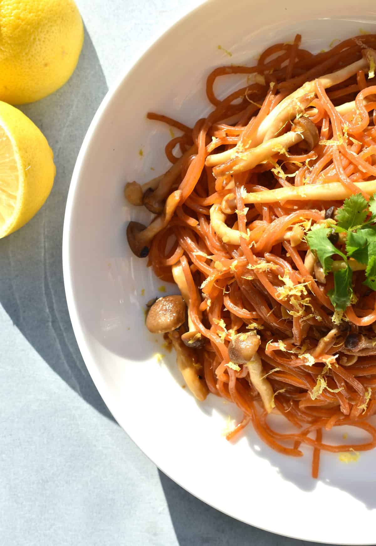 Soy-Butter Carrot Noodles with Mushrooms in a bowl with fresh lemons beside