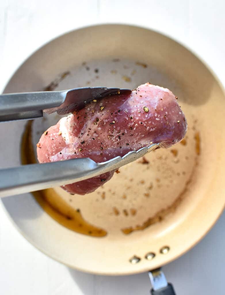 raw duck breast in tongs ready to go in a hot pan