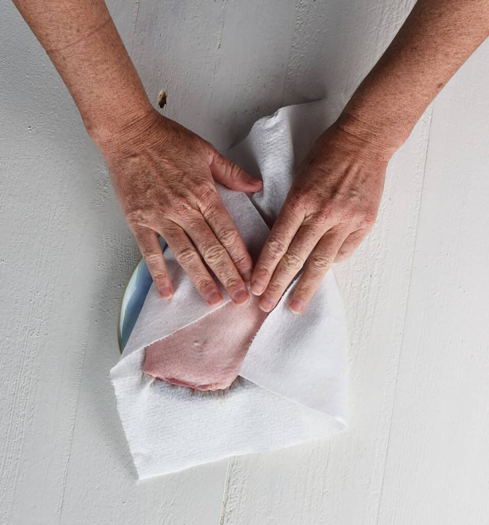 duck breast being patted dry with kitchen towel