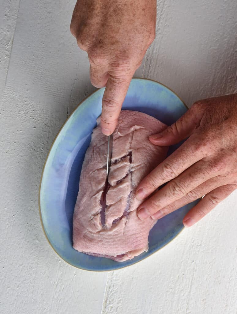 a duck breast being scored with a knife