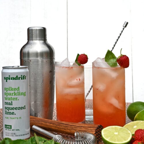 two strawberry cocktails with a shaker, can of sparkling water and limes