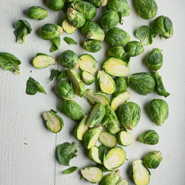 Whole and halved Brussels sprouts on a wooden surface.