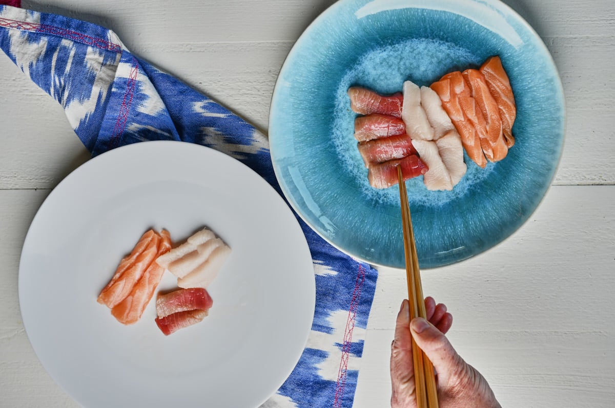 person plating sashimi on a blue plate