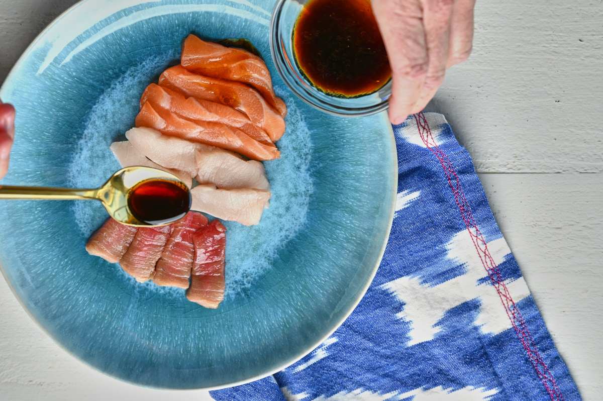 Soy sauce being drizzled on sashimi fish on a blue plate