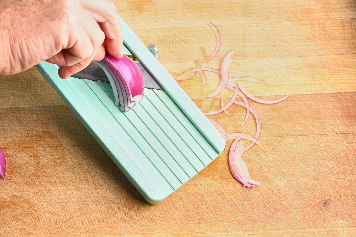 slicing a red onion on a mandolin
