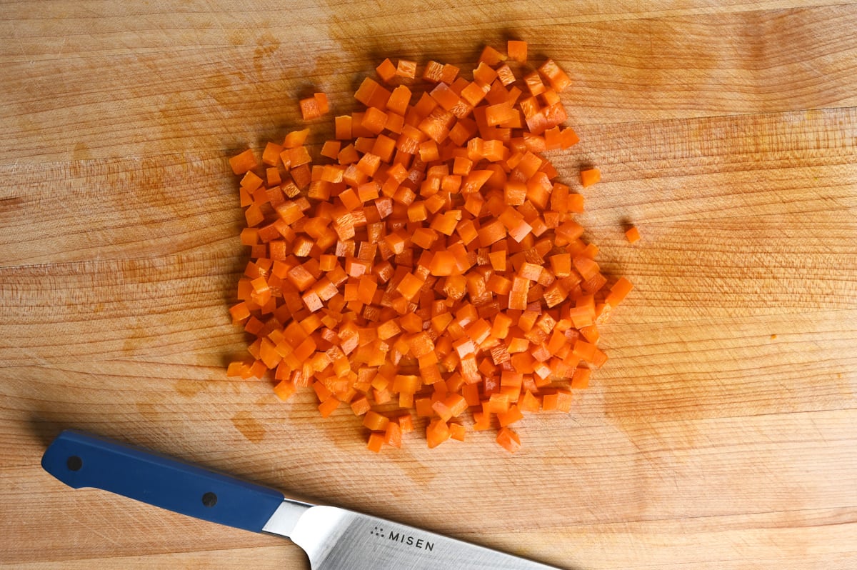 Diced Orange Bell Pepper pieces centered on a wooden cutting board