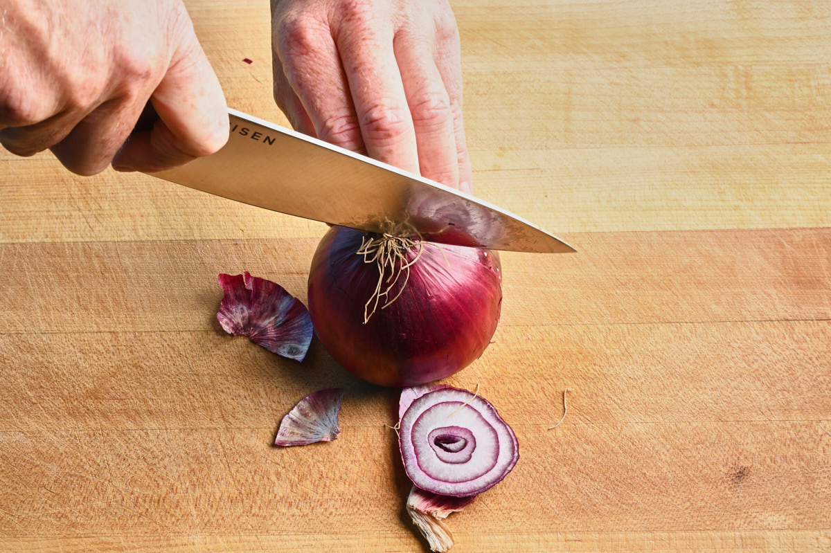 a red onion being sliced down the middle with a chef's knife