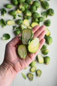 Hand holding three halved Brussels sprouts over a pile of fresh sprouts.