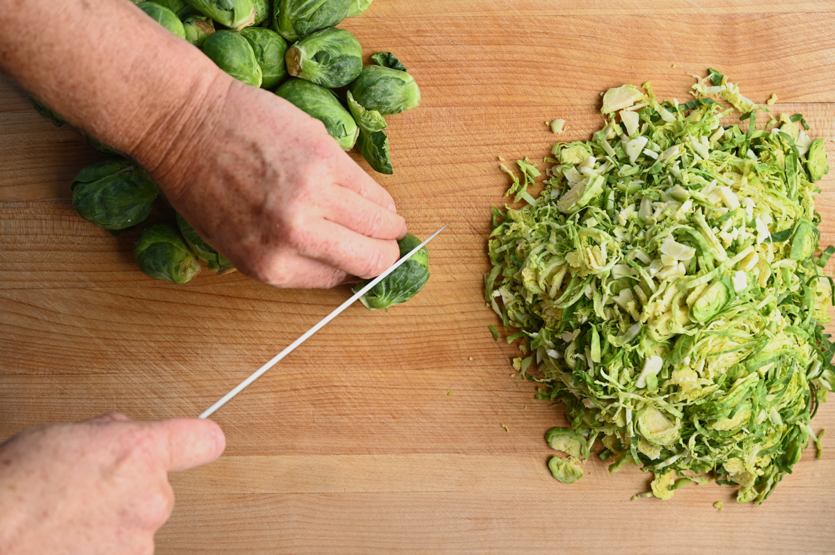 chopping brussel sprouts on a wooden cutting board