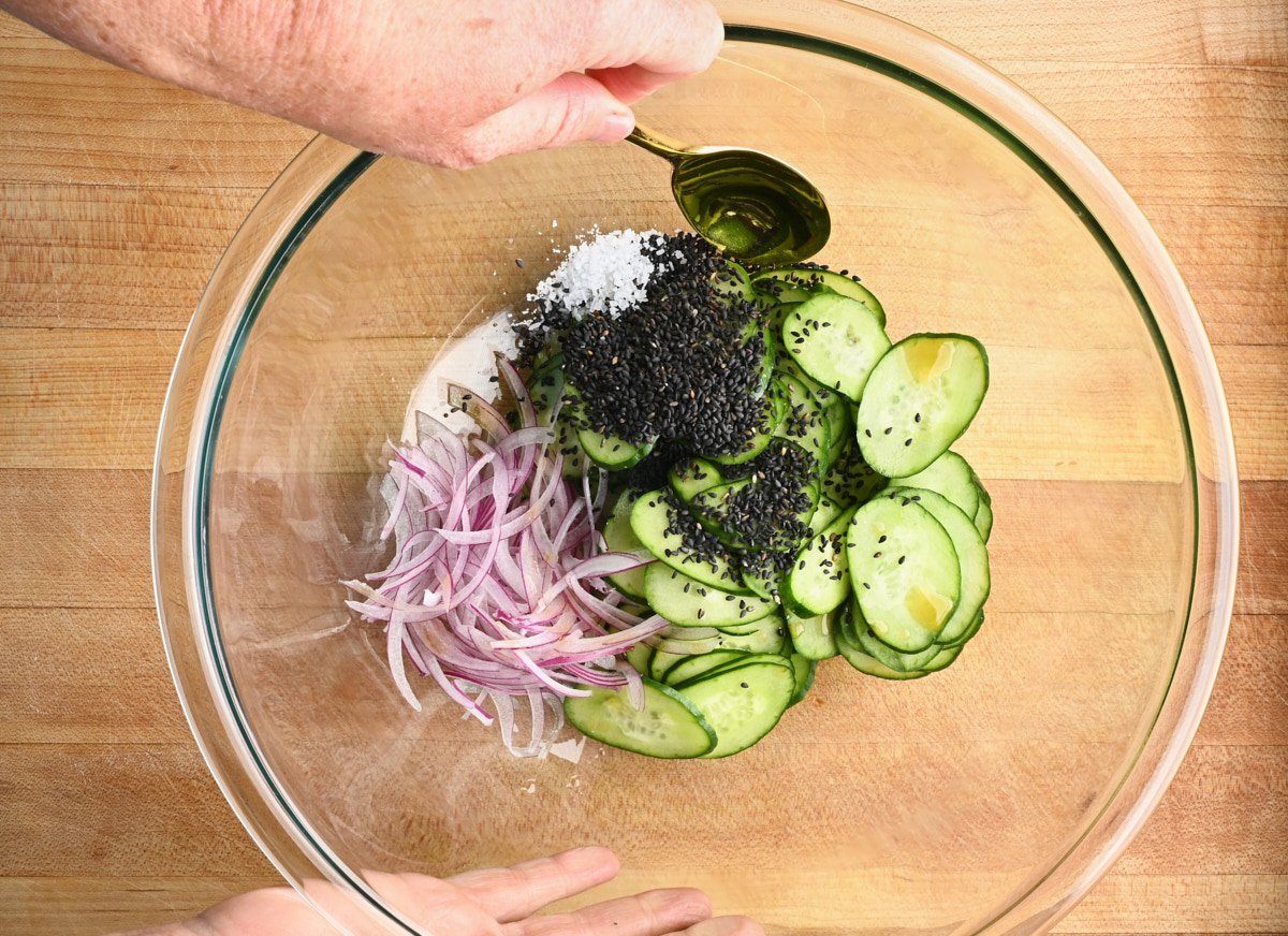 red onion, black sesame seeds, sliced cucumbers and salt in a glass bowl.