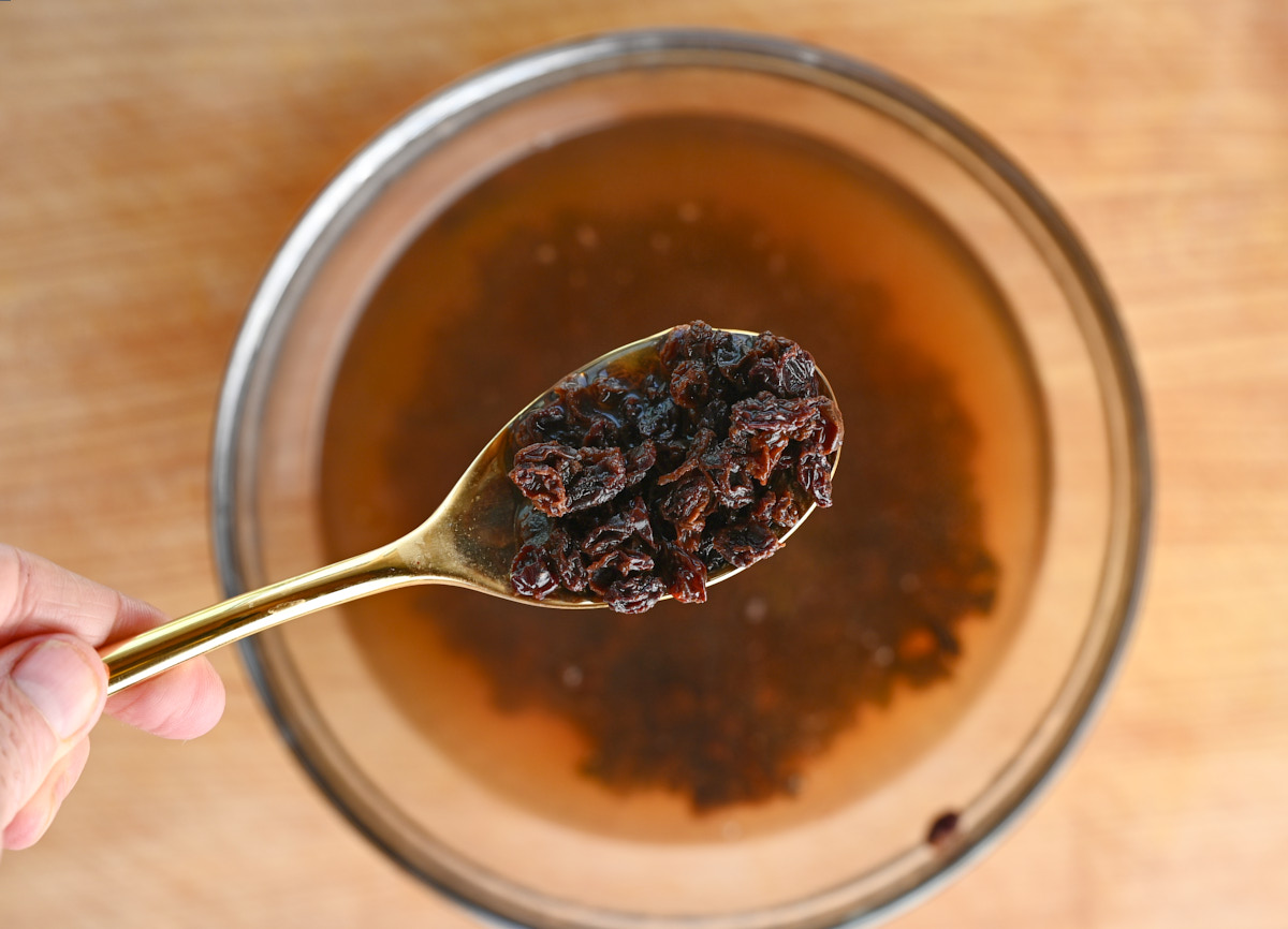 rehydrated currants on a gold spoon being held over a blurred bowl of currants