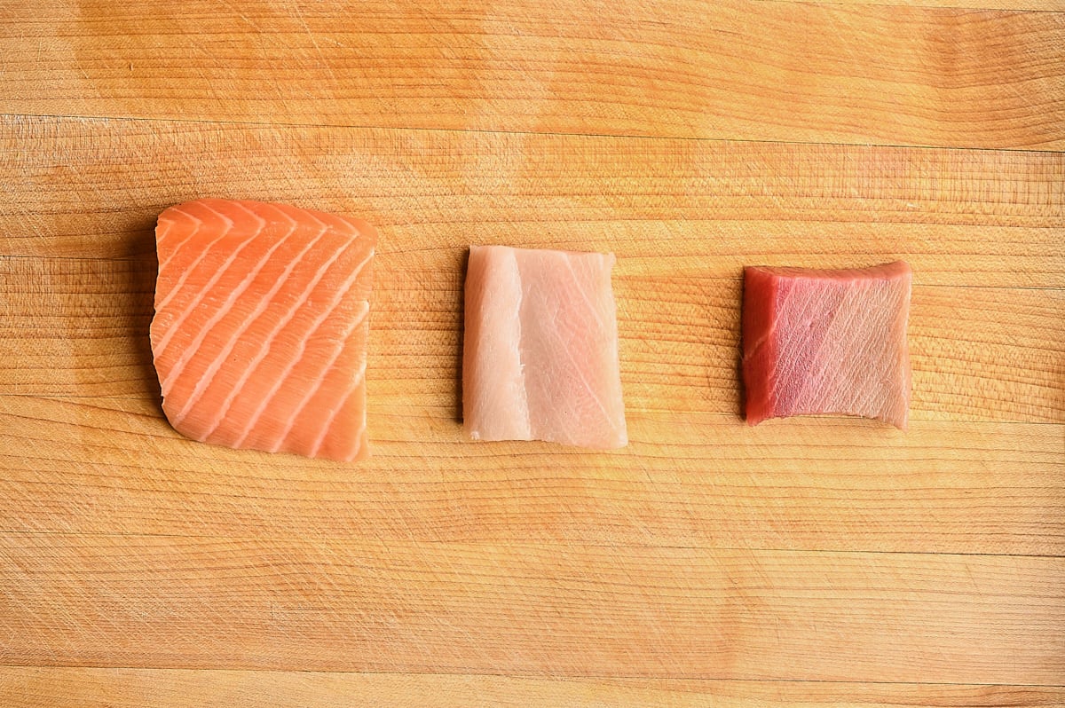 pieces of Salmon, yellowtail, and Toro on a wooden cutting board