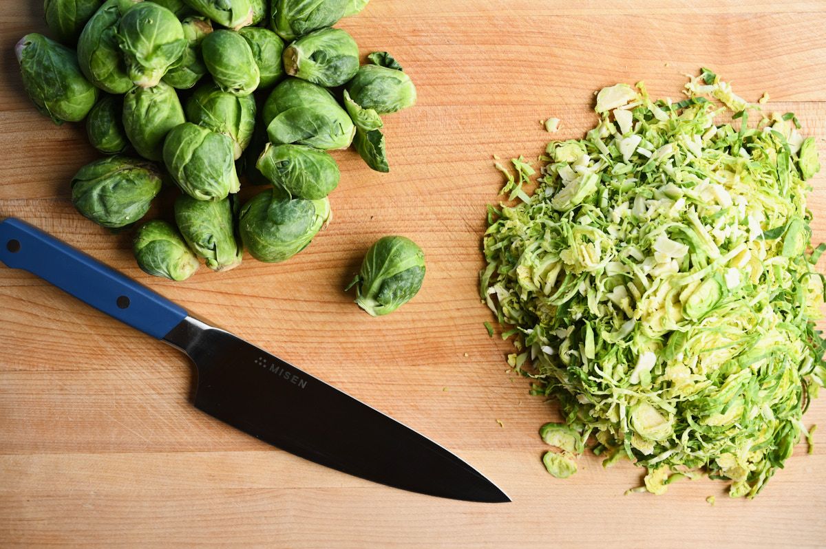 Halved and chopped Brussel Sprouts on a cutting board with a knife