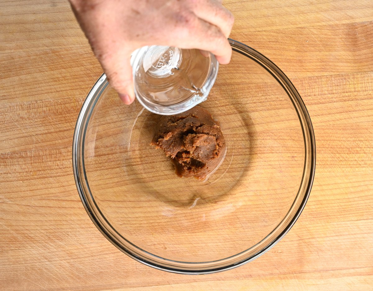 boiling water being poured over miso paste in a glass mixing bowl