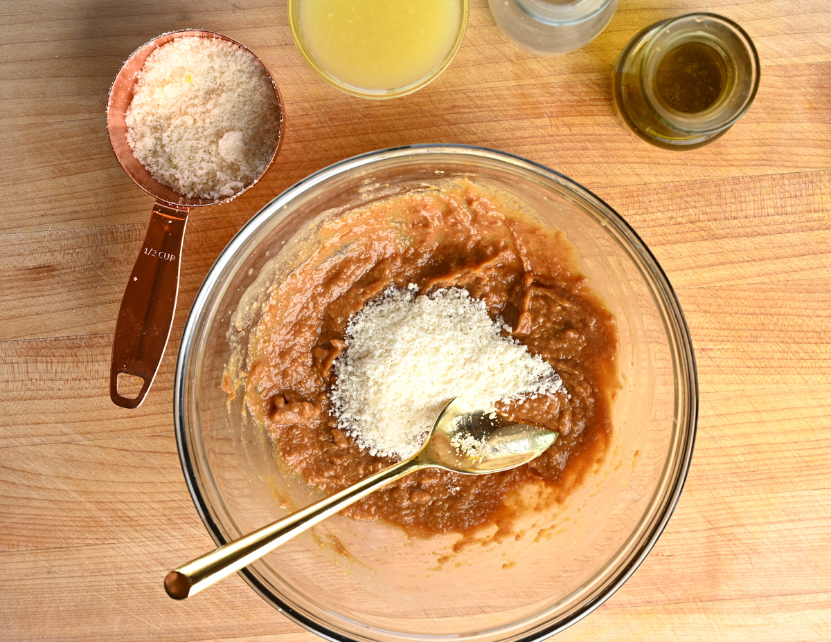 grated Parmigiano Reggiano being added to miso sauce with other ingredients sitting besides