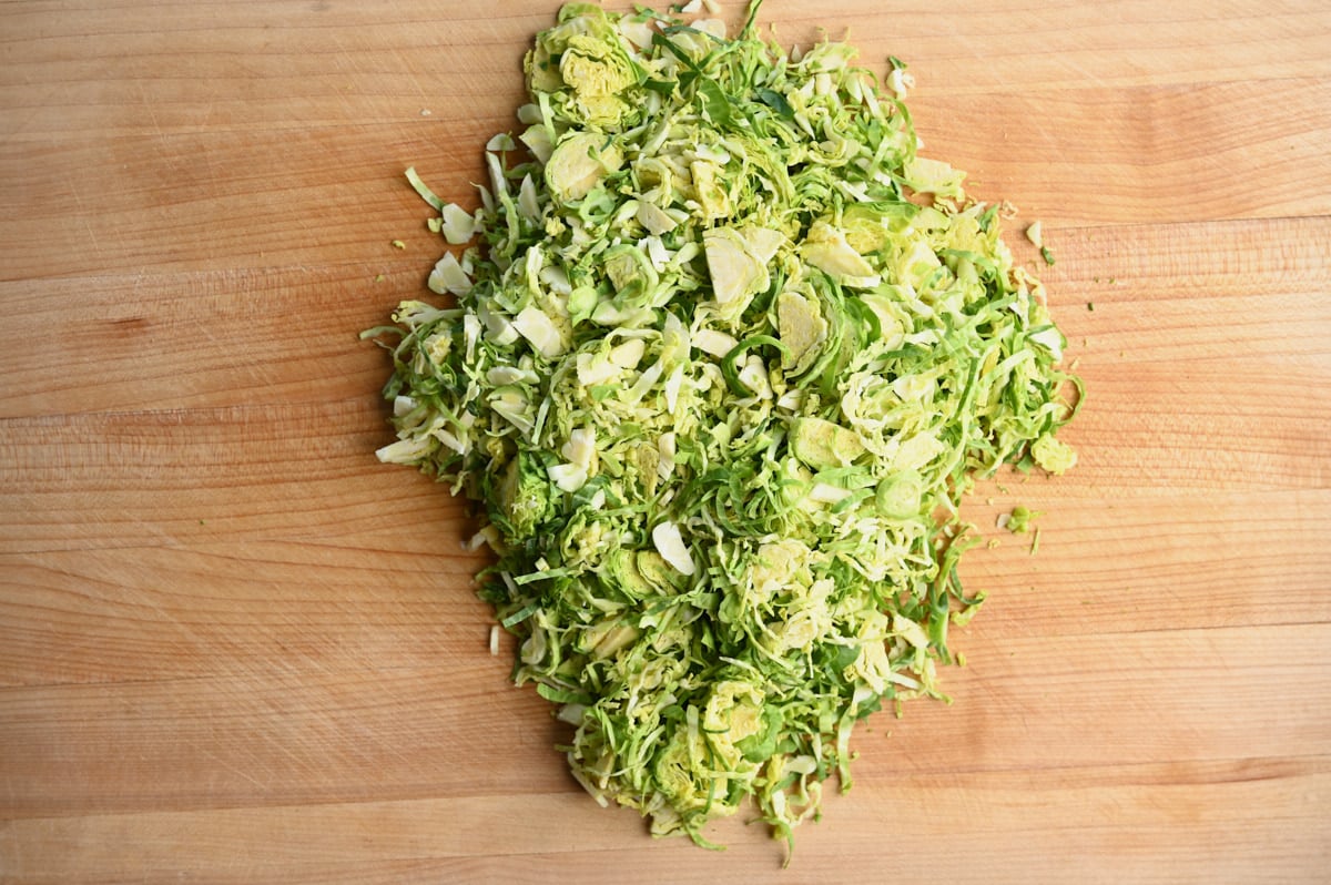 A pile of chopped Brussel Sprouts in the middle of a wooden cutting board