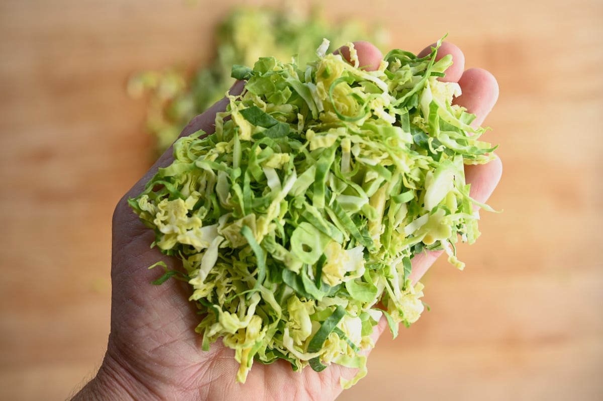 Chopped Brussel Sprouts in the palm of a hand against a wooden cutting board.