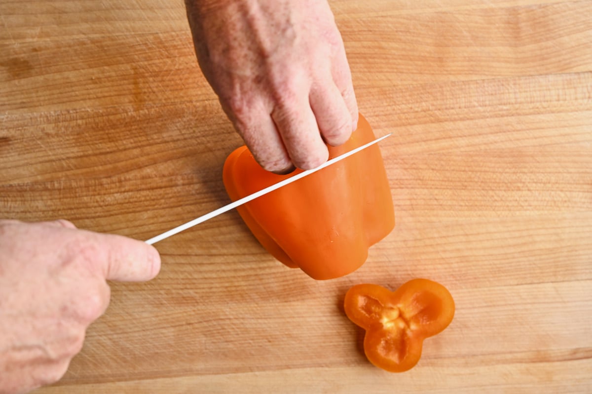 Hands cutting the ends off an orange bell pepper