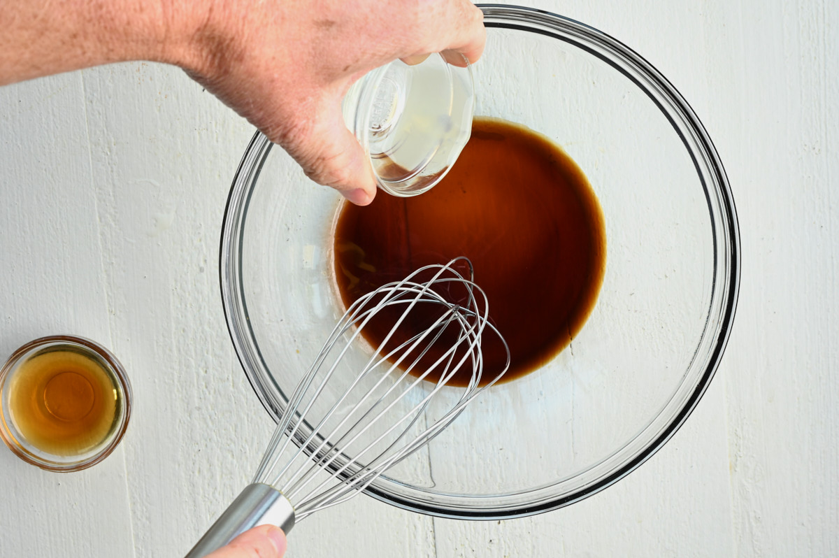 lemon juice being added to soy sauce in a glass bowl with a whisk