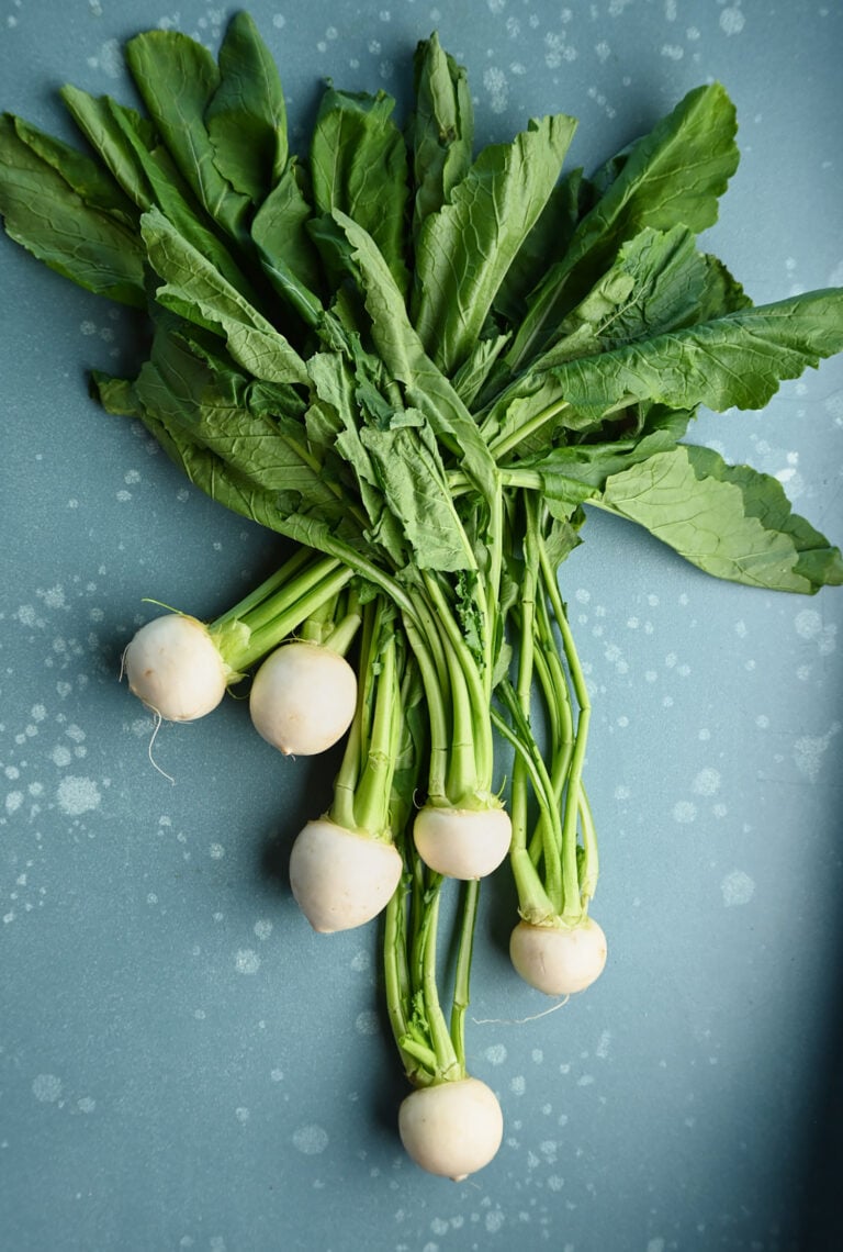 Tokyo turnips with their greens attached, arranged on a blue surface board.