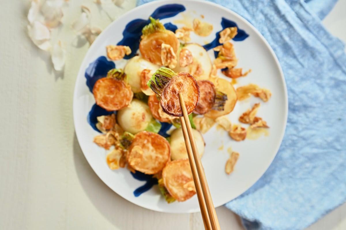 close up on a turnip between chop sticks being held over a plate of turnips