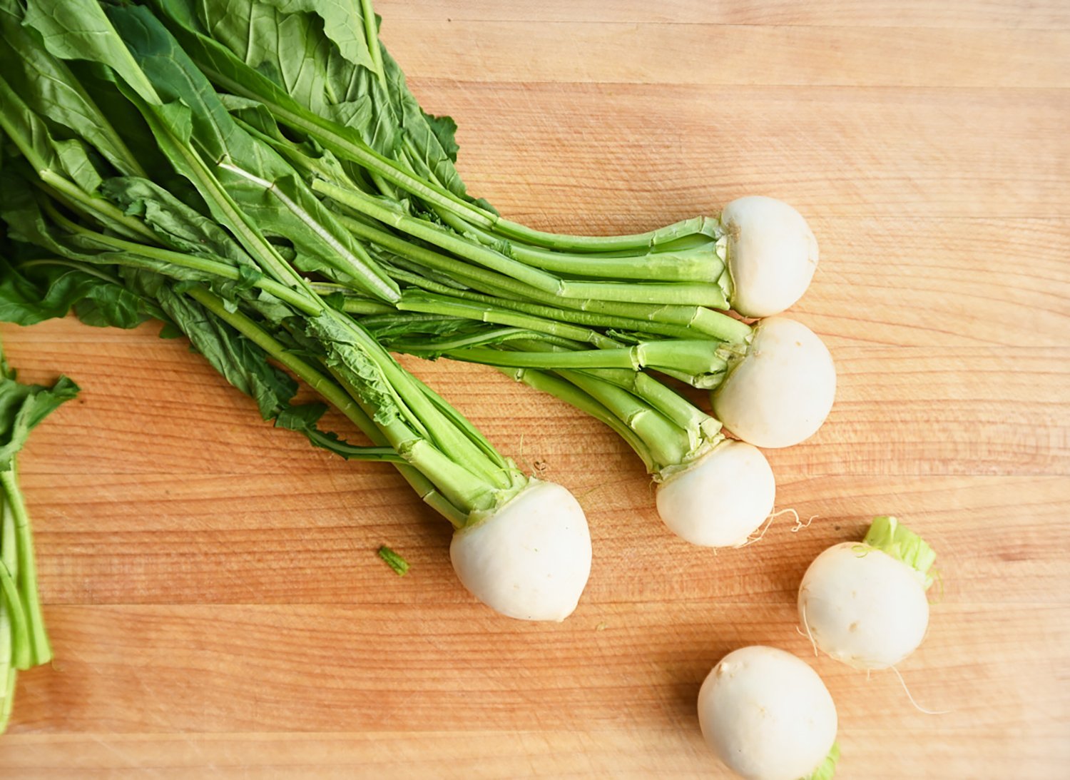 six turnips on a wooden cutting board.